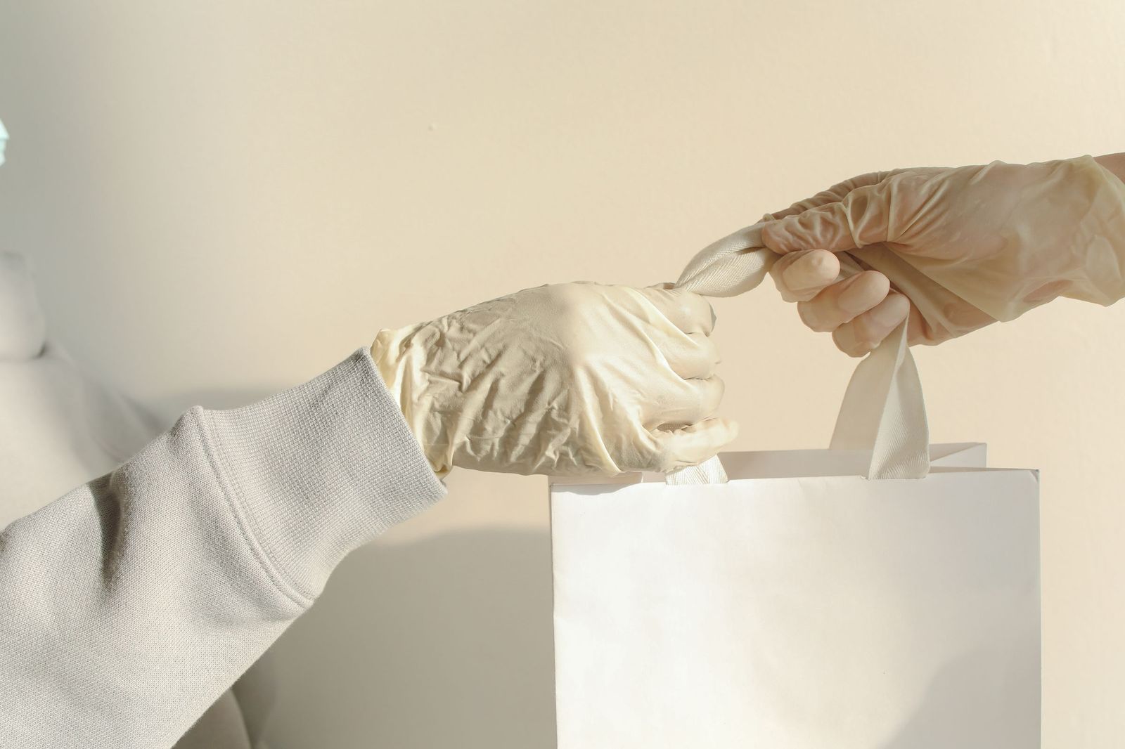 Two gloved hands passing a white paper bag from one person to another