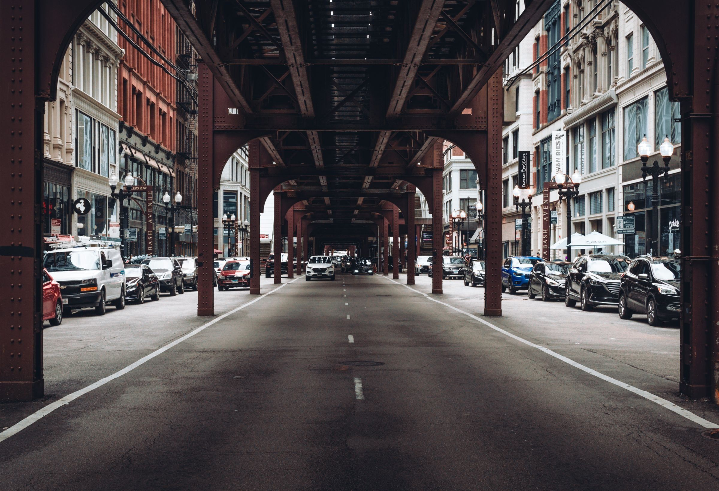 A downtown Chicago street under the elevated train tracks, with a white van parked at the curb